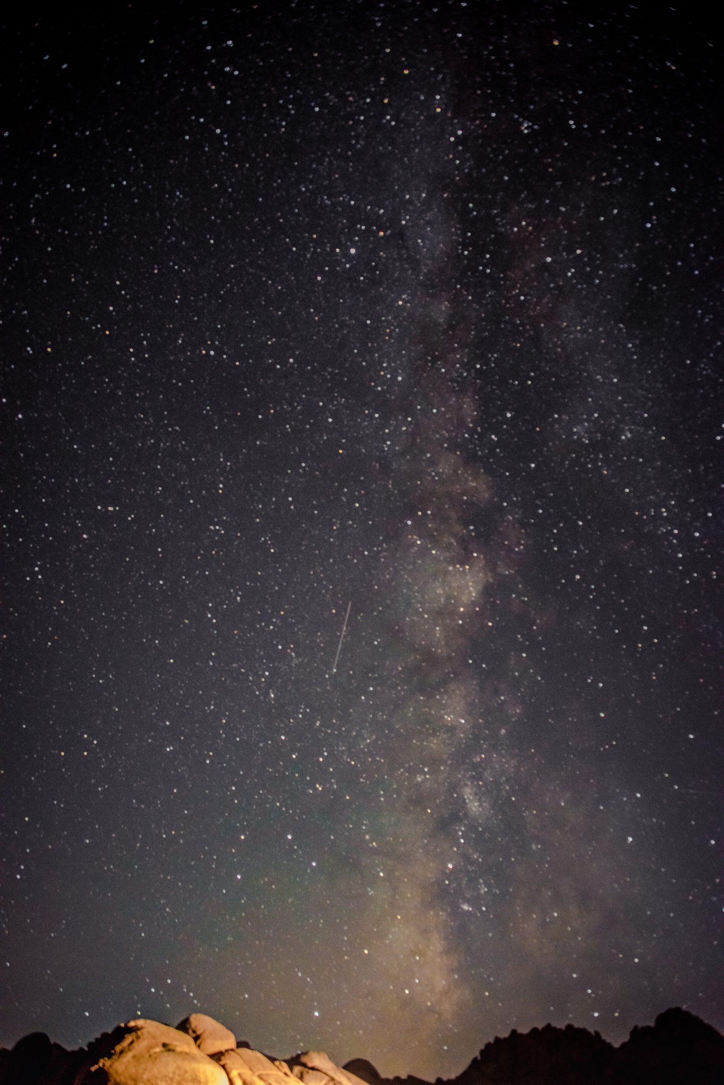 Giant granite boulders lit up under the massive scale of the Milky Way in Joshua Tree California. The colors of the solar system shine through the dark night to shine on everything in sight. Reminding one of how large everything is.